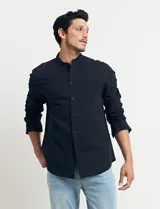 Camisa de cuello mao y manga larga, confeccionada en una mezcla de lino y algodón. Presenta un diseño de corte recto con botones en tono natural y un bolsillo pequeño en el pecho.