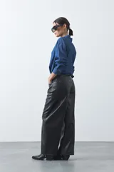 Pantalón de cuero sintético con fit barrel, de silueta amplia con volumen en las piernas y botamanga levemente entallada. Presenta bolsillos laterales y cierre frontal.