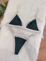 Conjunto de lencería compuesto por bralette triangular y tanga, confeccionado en algodón color verde inglés con detalles de encaje en tono nude. El bralette cuenta con breteles ajustables y broche regulable, mientras que la tanga presenta laterales ajustables.