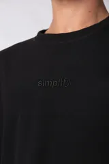 Remera negra de corte oversize con cuello redondo y mangas cortas. Presenta la palabra "simplify" bordada en el pecho en el mismo tono. Confeccionada en tejido de punto con textura sutil tipo waffle.