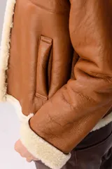 Campera tipo gamulán de cuero color tostado con interior y detalles en piel sintética color crema. Presenta cuello solapa, cierre frontal y mangas largas con puños de piel.