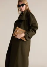 Abrigo tipo trench de diseño oversize y corte recto, color verde militar. Presenta cuello de solapa ancha, cierre frontal de doble botonadura, cinturón desmontable con hebilla y bolsillos laterales. Incluye trabillas en los puños y forro interior.