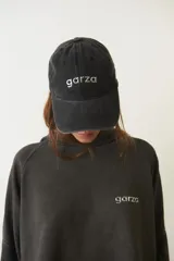 Gorra de gabardina negra con visera curva y aplique metálico plateado con la palabra "garza" en el frente.