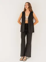 Pantalón negro de lino, tiro alto, corte palazo, con elástico en la pretina trasera, cierre delantero y broche interno. Tiene bolsillos laterales, dobladillo invisible y tajos a los costados.