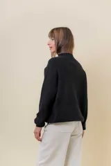 Sweater tejido de punto color blanco, con cuello alto y diseño en relieve tipo chevron en la parte frontal. Presenta un calce holgado con terminaciones acanaladas en puños y ruedo.