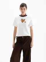 Remera de jersey pesado color blanco, con cuello redondo en contraste negro y estampa central de un corazón con diseño animal print atravesado por una flecha.