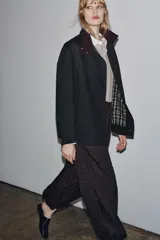 Chaqueta negra de la colección Zara Woman, confeccionada en hilatura con mezcla de algodón. Presenta un cuello alto brillante en contraste de color marrón oscuro, manga larga, bolsillos delanteros y pespuntes marcados. El forro interior es a contraste y el cierre frontal es con botones.