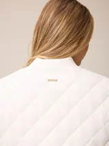 Chaleco acolchado de diseño matelassé con cierre frontal completo, cuello tipo bomber y bolsillos laterales. Presenta un pequeño bordado decorativo en la parte inferior.