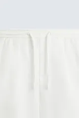 Bermuda negra de corte recto, con cintura elástica ajustable mediante cordón, pliegues frontales y bolsillos de vivo en la espalda. El bajo tiene un dobladillo vuelto.