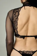 Conjunto de lencería negro compuesto por un top corto de terciopelo con cuello alto y mangas largas de microtul transparente con detalles de encaje, y una tanga regulable a juego con detalles de encaje y microtul.
