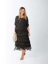 Vestido midi de seda italiana color negro, diseño dos en uno con capa superior de calce amplio, falda con volados y forro interior de algodón elastizado.