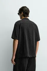 Camisa de corte relajado con cuello bowling y manga corta. Confeccionada en tejido fluido con textura jacquard de patrón geométrico y cierre frontal de botones.