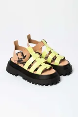 Sandalia tipo gladiadora con plataforma track negra. Presenta un diseño bicolor con tiras delanteras en color amarillo neón y talón con tira ajustable en color beige. Incluye hebilla metálica negra.