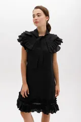 Vestido corto de lino color negro, con silueta recta y largo por encima de la rodilla. Incluye un cuello removible con volados y lazo, y detalles de volados en las sisas y el ruedo.