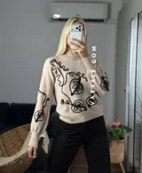 Sweater de tejido de punto con cuello redondo y diseño de bordado lineal en contraste que forma motivos orgánicos y florales. Presenta un corte clásico y mangas largas.