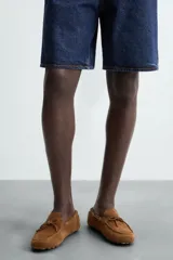 Mocasín casual de cuero color marrón claro con acabado serraje, horma redonda, detalle de lazo en el empeine y suela de goma.