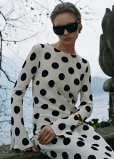 Vestido largo color crema con estampado de lunares negros, de corte ajustado, cuello redondo y mangas largas acampanadas.