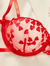 Conjunto de lencería rojo de dos piezas, confeccionado en tul semitransparente con bordados de corazones. Incluye corpiño con copa armada y bombacha colaless ajustable con tiras laterales terminadas en lazo.