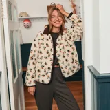 Chaqueta de sherpa color crema con estampado floral en tonos marrones, amarillos y verdes. Tiene cuello camisero y ribete de pana marrón.