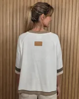 Buzo de punto negro con diseño holgado, mangas codo y detalles en tono tostado y blanco en el cuello redondo, puños y ruedo.