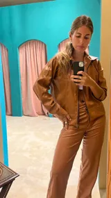 Campera marrón de cuero sintético con cierre frontal, cuello camisero y costuras decorativas en hilo blanco.