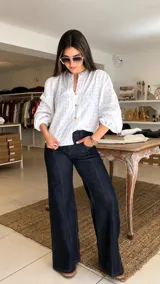 Camisa blanca de broderie con cuello redondo, cierre frontal con botones de madera y mangas largas abullonadas con puños elásticos.