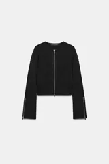 Chaqueta de punto color negro, con cuello redondo, manga larga con cremalleras en los puños y cierre frontal con cremallera.