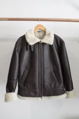 Campera tipo bomber de cuero genuino color negro, con interior y cuello de piel sintética negra. Presenta cierre frontal metálico, bolsillos laterales y puños con terminación en tejido acanalado.