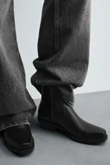Bota estilo cowboy de caña media, color negro, con punta cuadrada, tacón bajo y cierre lateral.