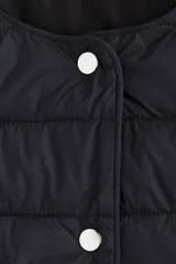 Campera acolchada negra, de nylon guateado, con cuello redondo y cierre frontal de botones a presión. Presenta bolsillos laterales discretos y elástico fino en los puños.