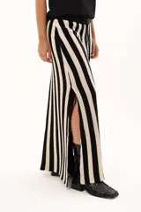 Pollera larga de tejido de punto con diseño de rayas verticales en color negro y crudo. Presenta una pretina elástica con cordón de ajuste y tajos laterales profundos que aportan movimiento.