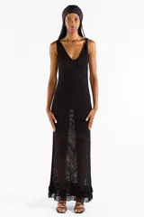 Vestido largo negro de punto abierto con sutil brillo de lúrex, escote en V y detalles de flecos en el ruedo.