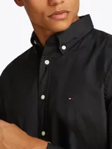 Camisa negra de popelina con cuello abotonado, cierre frontal con botones, manga larga con puños abotonados y logo de Tommy Hilfiger bordado en el pecho.