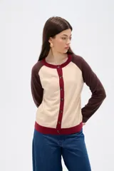 Cardigan de punto con diseño color block, presenta cuerpo en color celeste, mangas en color bordó y detalles de botones y bordes en color rosado. Posee cuello redondo y mangas largas.