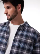 Camisa de manga larga con diseño a cuadros en tonos azules, grises y blancos. Presenta cuello camisero, cierre frontal con botones y un bolsillo en el pecho con etiqueta de la marca.