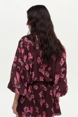 Blusa bordó con estampado floral en tonos rosados, confeccionada en algodón Swiss Dot, con mangas largas abullonadas y escote en V con botones frontales.