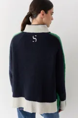 Campera de lana con cierre frontal de doble cursor y cuello alto. Presenta un diseño en bloques de color azul marino, verde y crema, con detalles de tejido trenzado en las mangas y bolsillos laterales con contraste.