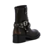 Bota de caña baja de cuero color marrón, con taco cuadrado, puntera redondeada y diseño estilo biker. Cuenta con dos tiras con hebillas metálicas y ojalillos decorativos alrededor del empeine.
