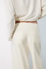 Pantalón fluido de color blanco, de tiro alto con trabillas y pliegues en el delantero. Cuenta con bolsillos laterales, cierre frontal con cremallera, botón interior y gancho metálico.