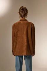 Blazer de gamuza color marrón con cuello solapa, corte holgado y detalle de tachas metálicas en solapas, bolsillos delanteros y puños.