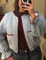 Campera acolchada de color celeste claro con detalles de ribetes en color bordó. Presenta cierre frontal, mangas largas con puños elásticos y dos bolsillos delanteros con bordados de figuras de caballos en color bordó.