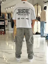 Remera gris oscuro con corte boxy fit de manga corta y cuello redondo. Cuenta con un diseño gráfico frontal con la palabra "CONCEPT" en grandes letras blancas delineadas y líneas decorativas horizontales y en las sisas.