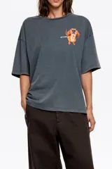 Remera de corte oversize color gris oscuro con efecto lavado, cuello redondo y manga corta amplia. Presenta un estampado pequeño de un perro salchicha con el logo de la marca en el pecho.