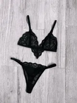 Conjunto de lencería compuesto por un bralette de encaje con diseño triangular y una bombacha tipo tanga a juego, ambos en color negro.