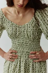 Vestido corto de algodón con estampado geométrico en tonos verdes y blancos. Cuenta con escote en V, mangas globo con elástico en los puños, cuerpo fruncido tipo nido de abeja en la cintura y falda con vuelo.