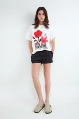 Remera de corte oversize y silueta boxy, color blanco, con cuello redondo y mangas cortas. Presenta una estampa frontal con diseño de flores en tonos rojos y rosados con efecto spray y tipografía negra.