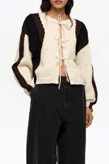 Cardigan de punto con diseño de bloques de color en blanco, negro y marrón, escote redondo y cierre frontal con múltiples lazos de tela.