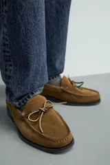 Mocasín de vestir para hombre confeccionado en piel con acabado en gamuza de color marrón, con punta redonda, suela oscura con ligero tacón y detalle de lazo en el empeine.