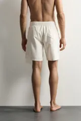 Short de baño largo en color beige, confeccionado en tejido técnico con tacto aterciopelado. Cuenta con cintura elástica ajustable con cordón, bolsillos laterales y detalle de bolsillo trasero, además de forro interior.