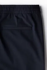 Jogger de vestir slim fit color azul marino, con pliegues adelante y atrás, elástico revestido con cordón ajustable en la cintura y bolsillos al bies.